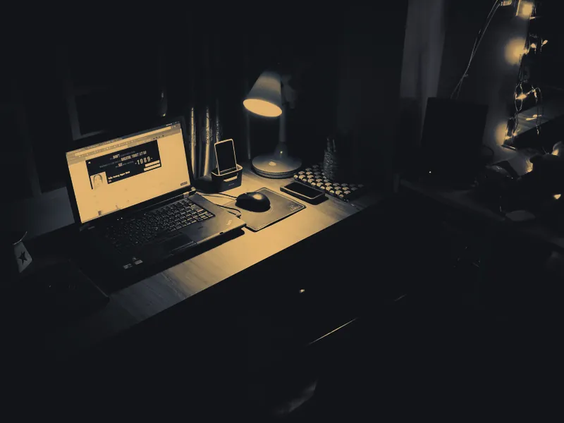 Mesa de trabalho com notebook aberto em ambiente escuro